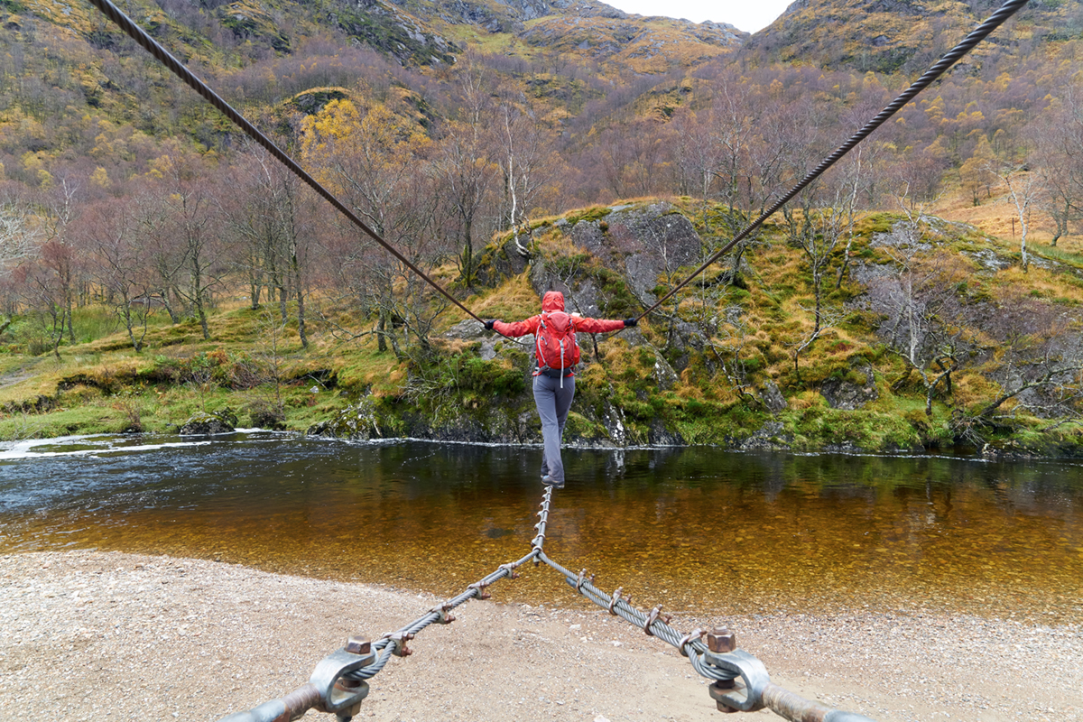 A hiker crossing the wire footbridge over the Water of Nevis. Glen Nevis, Scottish Highlands